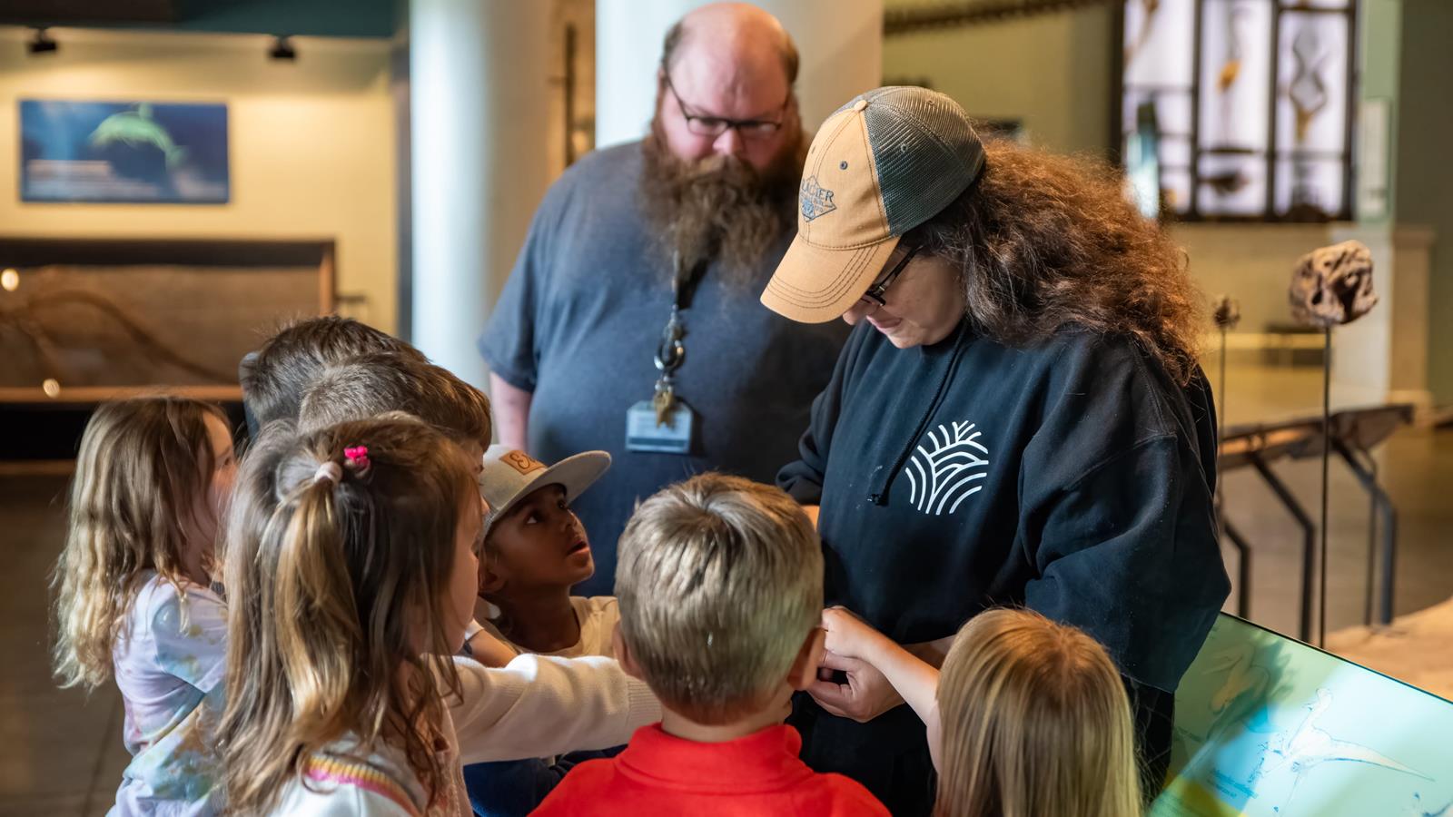A group of school children looking at a fossil being shown to them by two educators.
